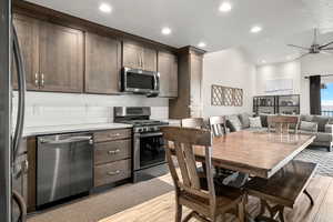 Kitchen with appliances with stainless steel finishes, dark brown cabinetry, a ceiling fan, tasteful backsplash, and light wood-style floors