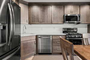 Kitchen featuring stainless steel appliances, decorative backsplash, and light stone countertops