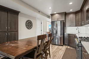 Kitchen with dark brown cabinetry, appliances with stainless steel finishes, recessed lighting, tasteful backsplash, and light wood finished floors