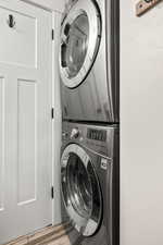 Laundry area with stacked washer / drying machine and wood finished floors