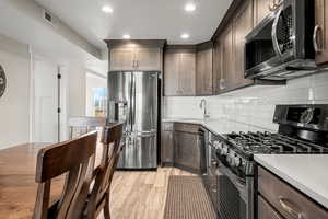 Kitchen with stainless steel appliances, dark brown cabinetry, decorative backsplash, light wood-style flooring, and recessed lighting
