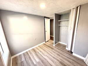 Unfurnished bedroom featuring a textured wall, a textured ceiling, a closet, and light wood-style flooring