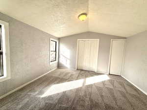 Unfurnished bedroom with a textured wall, vaulted ceiling, a textured ceiling, and carpet flooring
