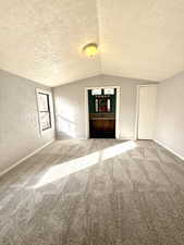 Carpeted empty room featuring a textured wall, a textured ceiling, and lofted ceiling