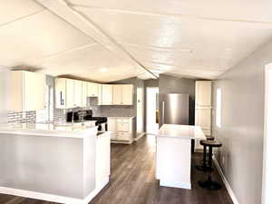 Kitchen with a peninsula, decorative backsplash, stainless steel appliances, white cabinetry, and a breakfast bar area