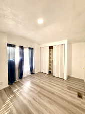 Unfurnished bedroom featuring a textured ceiling, wood finished floors, a closet, and lofted ceiling