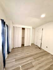 Unfurnished bedroom with light wood finished floors, a closet, a textured ceiling, and vaulted ceiling