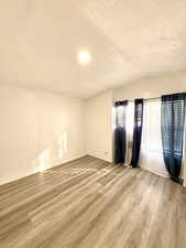 Empty room with vaulted ceiling, light wood-style flooring, and a textured ceiling