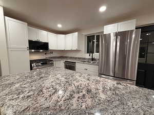 Kitchen featuring appliances with stainless steel finishes, light stone counters, white cabinets, and recessed lighting