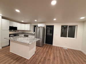 Kitchen with white cabinetry, light stone counters, stainless steel appliances, dark wood-style floors, and recessed lighting