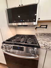 Kitchen view of stainless steel appliances, white cabinets, and light stone countertops