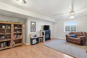 Living area featuring light wood-style floors, a ceiling fan, a textured ceiling, and a glass covered fireplace