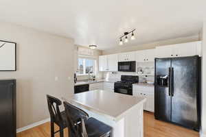 Kitchen featuring black appliances, light countertops, white cabinets, and light wood-style flooring