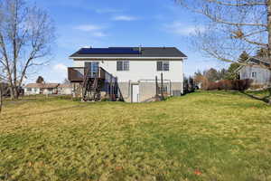 Rear view of property featuring stairway, roof mounted solar panels, a yard, and a deck