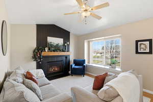 Living room featuring a large fireplace, lofted ceiling, a ceiling fan, and wood finished floors
