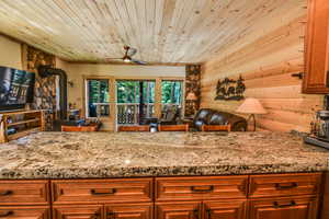 Kitchen featuring a wood stove, brown cabinets, open floor plan, light stone counters, and wooden ceiling