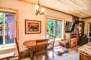 Dining space featuring a wood stove, plenty of natural light, wooden ceiling, hardwood / wood-style floors, and a chandelier