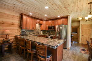 Kitchen with wooden ceiling, brown cabinets, stainless steel appliances, a peninsula, and a breakfast bar area