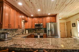 Kitchen with wood ceiling, appliances with stainless steel finishes, brown cabinets, recessed lighting, and dark stone countertops