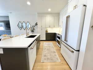 Kitchen with white appliances, white cabinets, light wood-style flooring, light stone countertops, and a kitchen island with sink