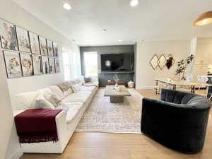 Living room with a textured ceiling, light wood-type flooring, and recessed lighting