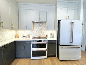 Kitchen featuring white appliances, light wood-style floors, light stone countertops, and decorative backsplash