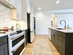 Kitchen with white appliances, under cabinet range hood, light wood-style floors, light stone countertops, and tasteful backsplash