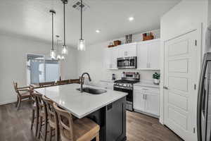 Kitchen with stainless steel appliances, white cabinets, decorative light fixtures, a kitchen island with sink, and light stone counters