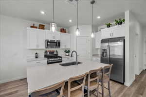 Kitchen featuring a kitchen breakfast bar, stainless steel appliances, decorative light fixtures, white cabinets, and light stone countertops