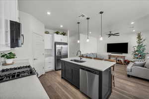 Kitchen with open floor plan, decorative light fixtures, stainless steel appliances, a center island with sink, and white cabinets