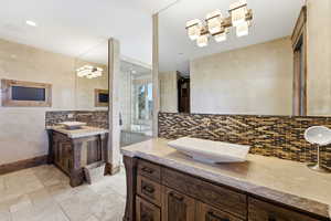 Full bathroom featuring two vanities, stone tile floors, decorative backsplash, and a stall shower