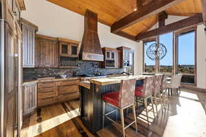 Kitchen featuring a chandelier, a breakfast bar, a wooden ceiling with exposed beams, glass insert cabinets, and a center island with sink