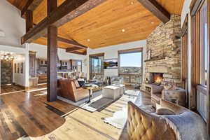 Living room featuring a stone fireplace, wood-type flooring, a wooden ceiling with exposed beams, and high vaulted ceiling