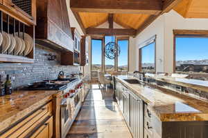 Kitchen featuring dark stone counters, range with two ovens, ventilation hood, backsplash, and dark wood-style floors