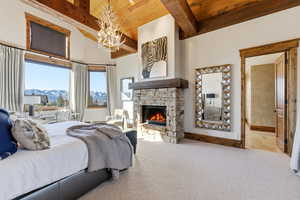 Bedroom featuring a stone fireplace, a wooden ceiling with exposed beams, carpet flooring, a chandelier, and a mountain view