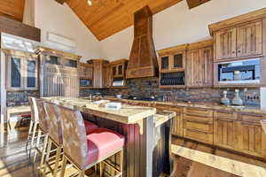 Kitchen featuring high vaulted ceiling, wood ceiling, an island with sink, glass insert cabinets, and a kitchen bar