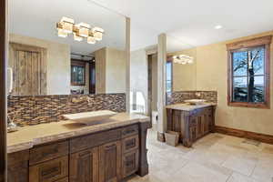Bathroom featuring vanity, stone tile flooring, tasteful backsplash, and a chandelier