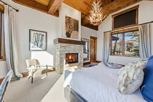 Carpeted bedroom with a stone fireplace and a wooden ceiling with exposed beams