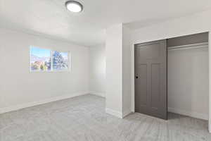 Unfurnished bedroom featuring light carpet, a closet, and a textured ceiling