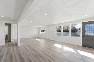 Unfurnished living room with light wood finished floors, a textured ceiling, and recessed lighting