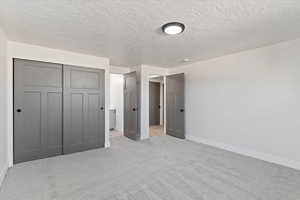 Unfurnished bedroom with a closet, a textured ceiling, and light carpet