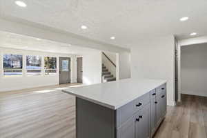 Kitchen featuring gray cabinets, a kitchen island, open floor plan, a textured ceiling, and light wood-style flooring
