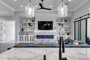 Living room featuring a glass covered fireplace, wood finished floors, crown molding, recessed lighting, and built in features