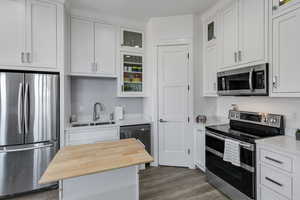 Kitchen with appliances with stainless steel finishes, white cabinetry, glass insert cabinets, and butcher block countertops