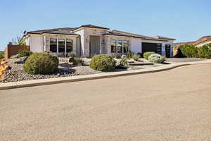 Prairie-style house with stucco siding, stone siding, an attached garage, and driveway