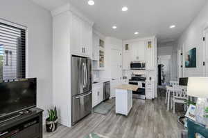 Kitchen featuring appliances with stainless steel finishes, white cabinets, glass insert cabinets, recessed lighting, and light wood-type flooring