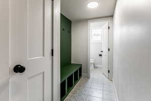 Mudroom from the garage featuring a textured ceiling and light tile patterned flooring with a built in bench.
