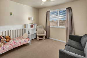 Bedroom with a nursery area, light colored carpet, and a ceiling fan