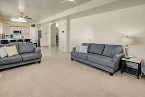 Living room with a ceiling fan, arched walkways, light colored carpet, and stairway