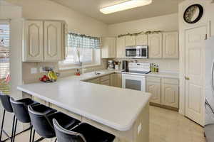 Kitchen featuring appliances with stainless steel finishes, a kitchen bar, light countertops, a peninsula, and cream cabinets